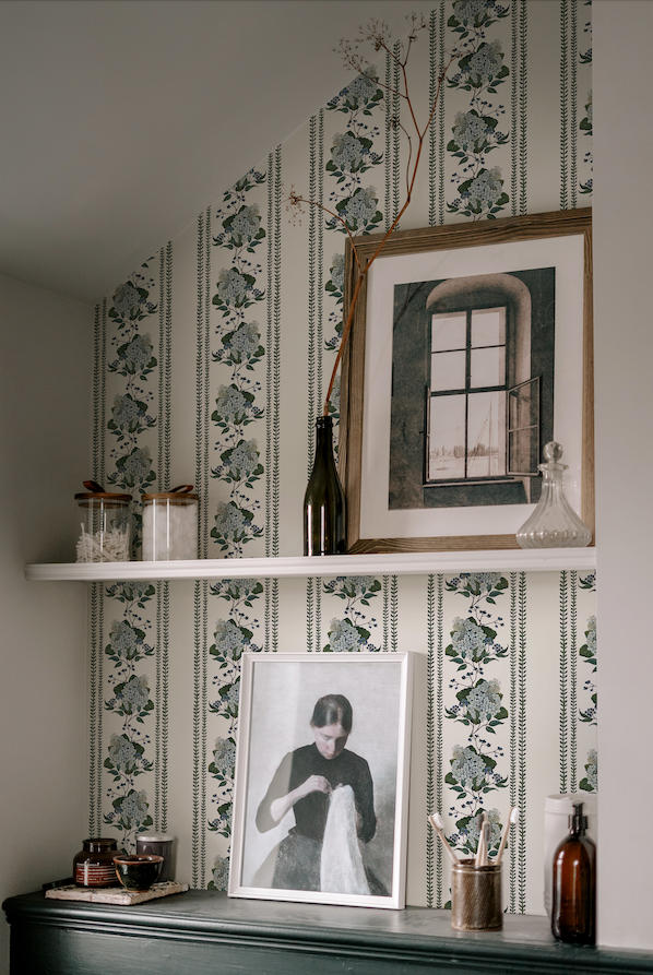 Decorative wall with floral wallpaper, framed pictures, and shelves with decorative items.
