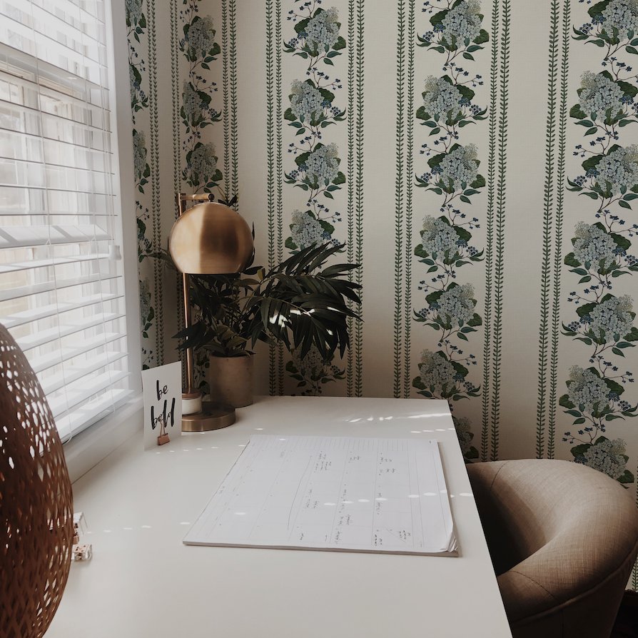 Home office with a desk, plant, and decorative wall paper.