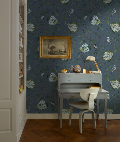 Room interior with a desk, chair, and framed picture against a floral wallpapered wall.