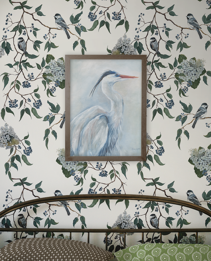 Framed artwork of a heron on a wall with floral and bird wallpaper.