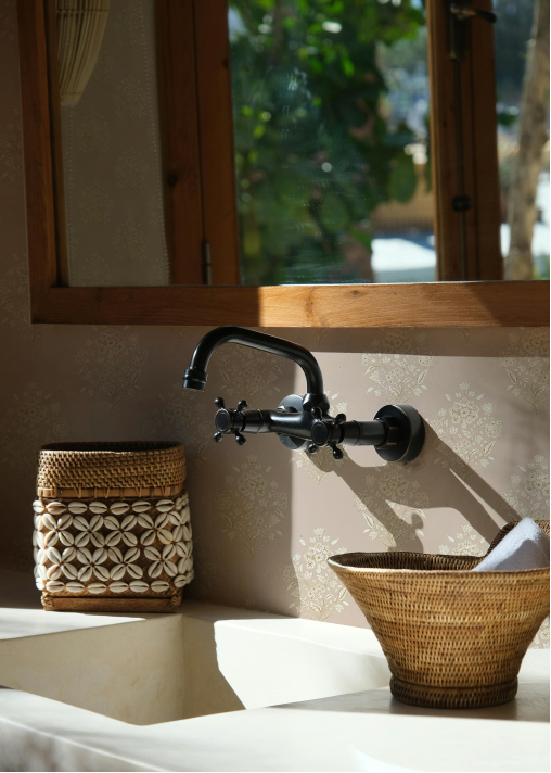 Bathroom setting with a black faucet, woven basket, and towel against a neutral wall.