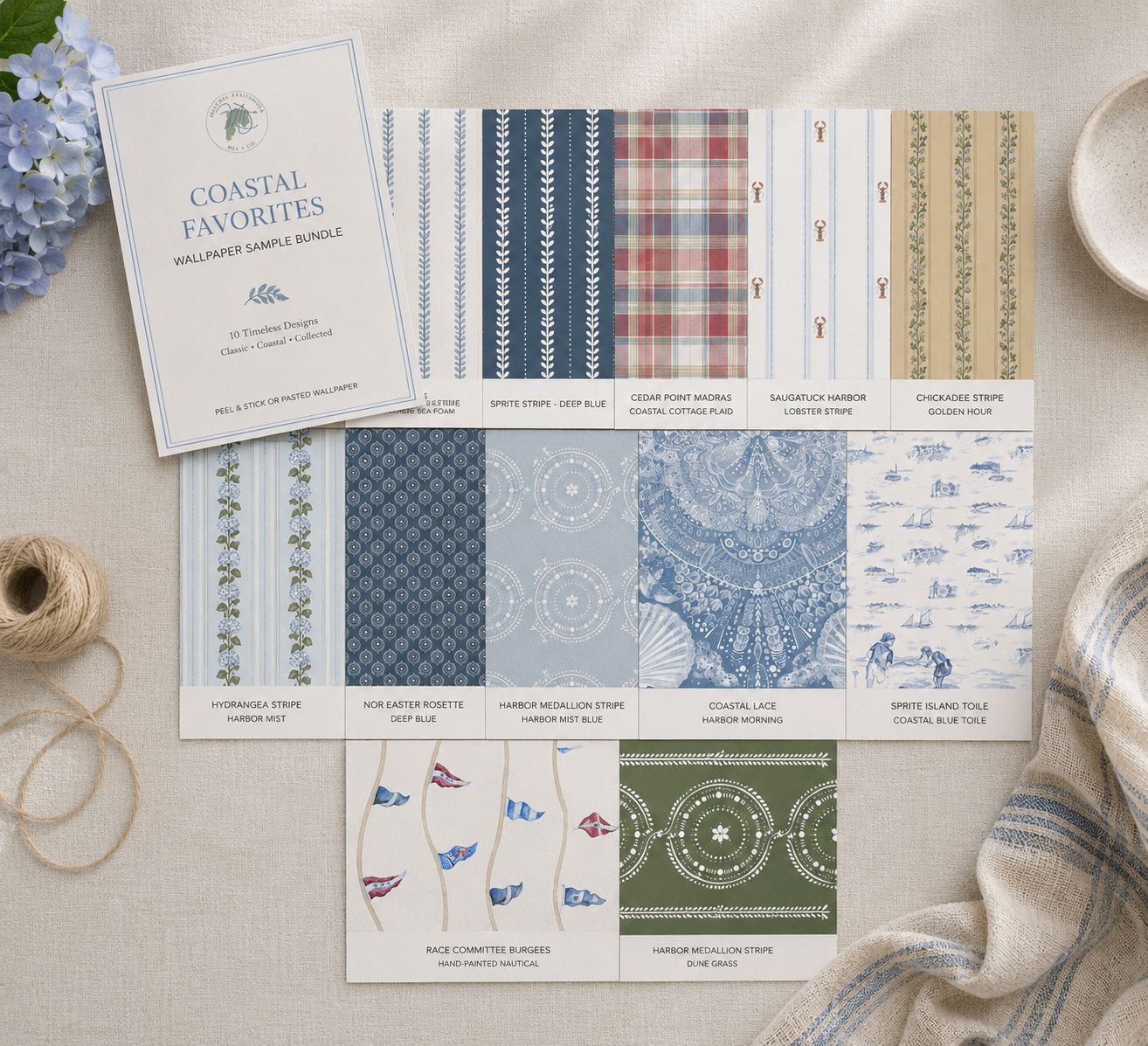 Collection of coastal-themed wallpaper samples with a brochure on a neutral surface.