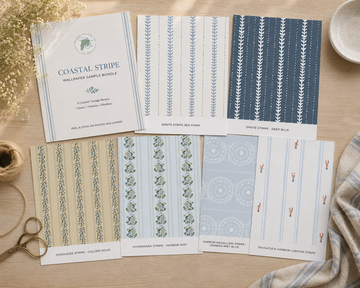 Collection of coastal stripe wallpaper samples on a wooden surface with a pair of scissors.