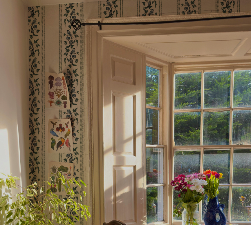 Decorative interior with floral wallpaper, a window view, and a vase of flowers.