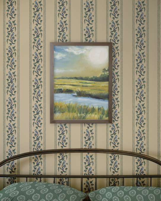 Framed painting of a landscape on a wall with floral-patterned wallpaper