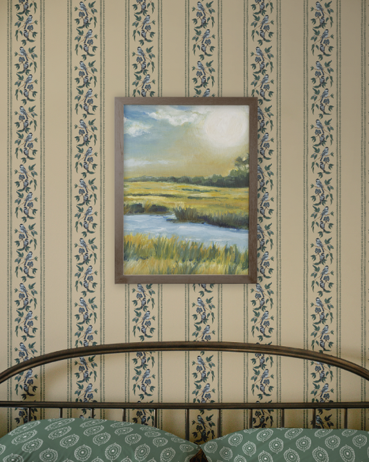 Framed painting of a landscape on a wall with floral-patterned wallpaper