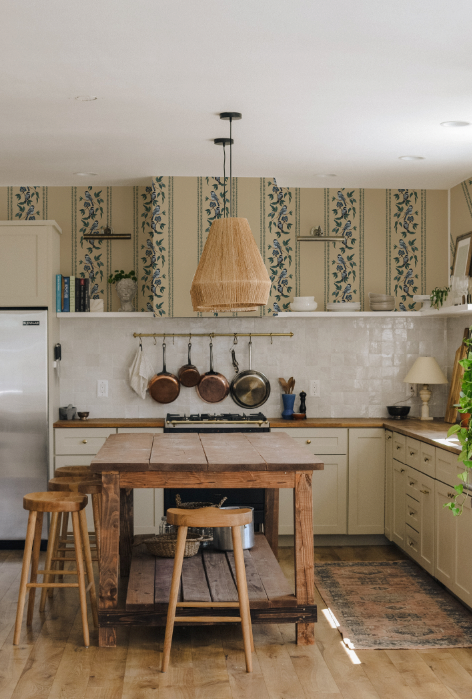 Kitchen with wooden island, stools, and decorative wallpaper.