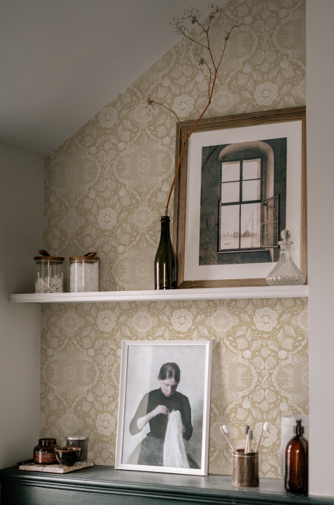 Decorative shelf with framed pictures and bottles against a patterned wall.