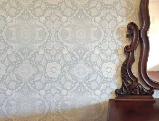 Decorative wooden mirror against a patterned wallpaper background