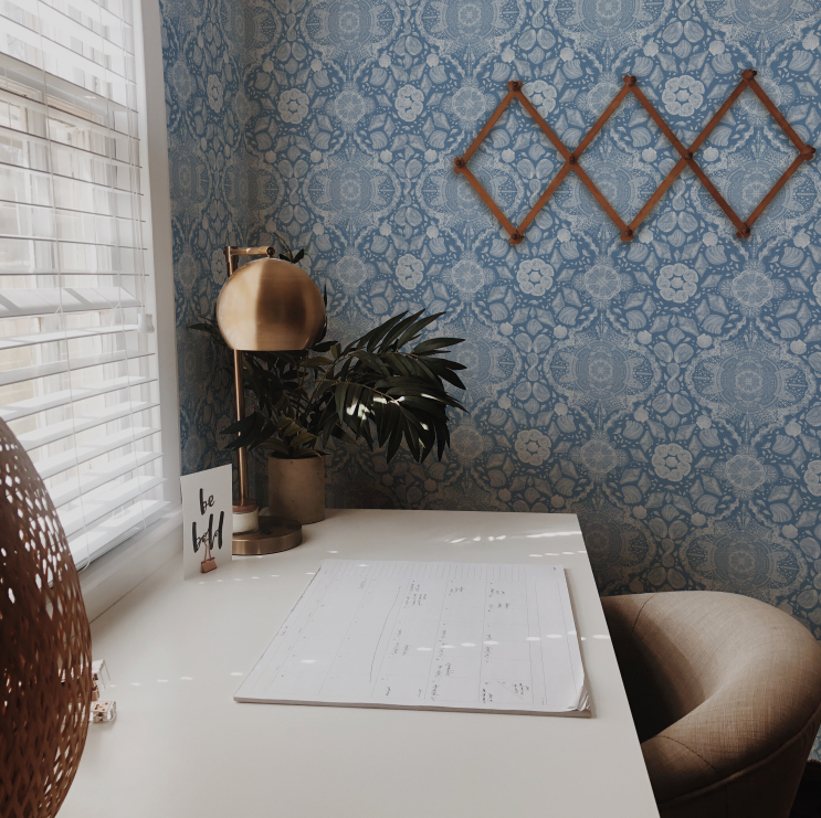 Home office with a desk, plant, and decorative elements against a patterned wall.