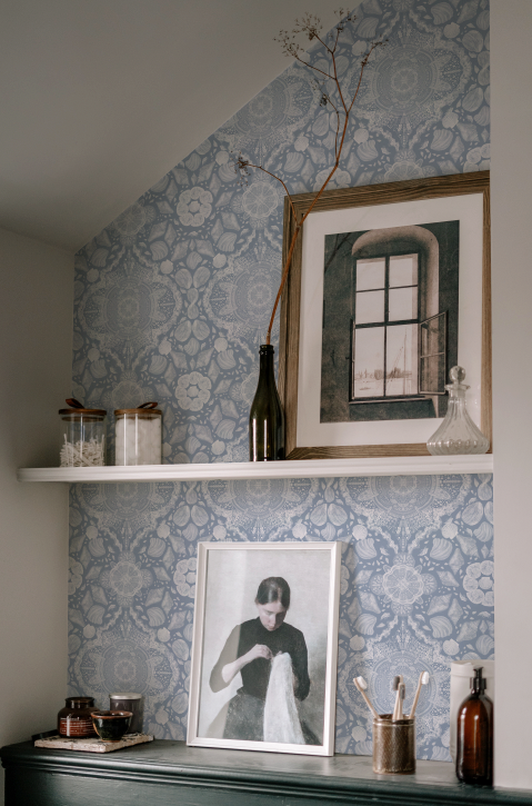 Decorative wall with patterned wallpaper, framed pictures, and small objects on a shelf.