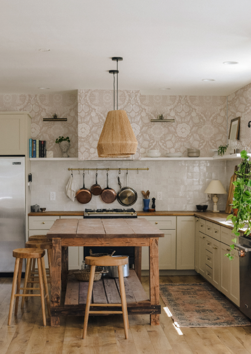 Kitchen with wooden table and stools, patterned wallpaper, and hanging pots.