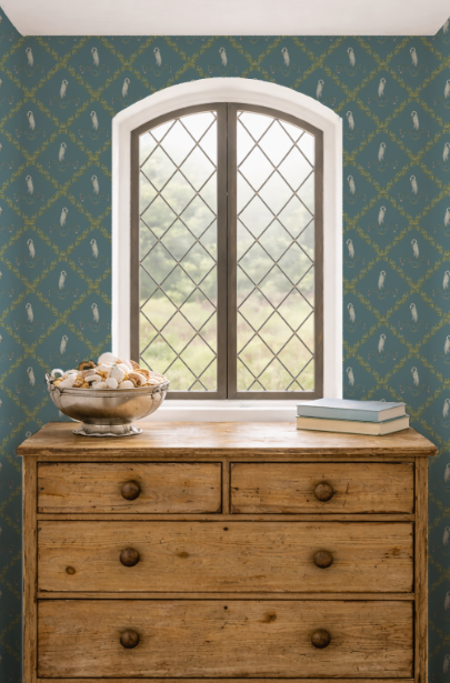 Wooden dresser with a bowl of seashells and books against a patterned wall with a window.