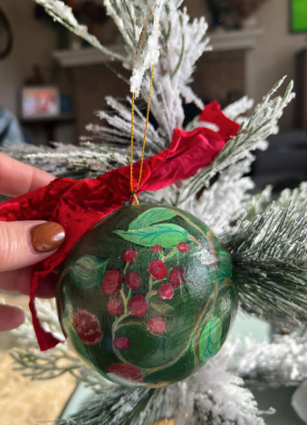 Decorative green ornament with floral design held against a Christmas tree.