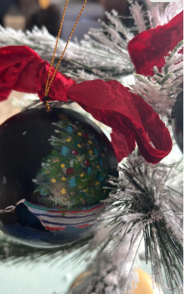 Decorative Christmas ornament with a tree design on a red ribbon against a blurred festive background.