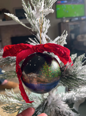 Decorative ornament with a red ribbon on a Christmas tree, with a blurred background of a television screen.