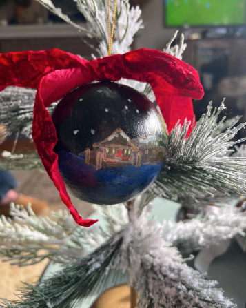 Decorative Christmas ornament with a red bow and a small cabin design on a tree.
