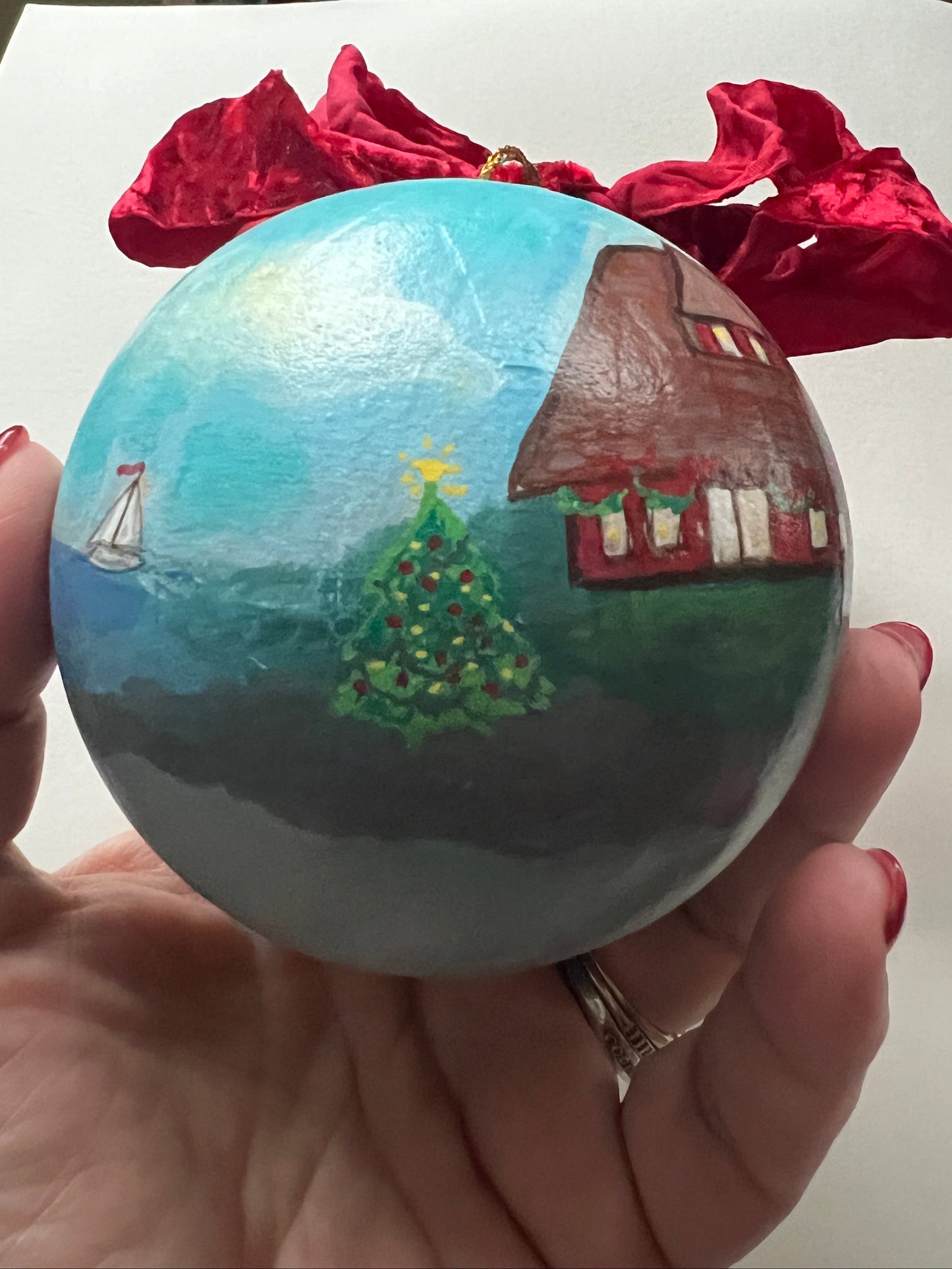 Hand holding a small painted globe with a house and tree design on a white surface.