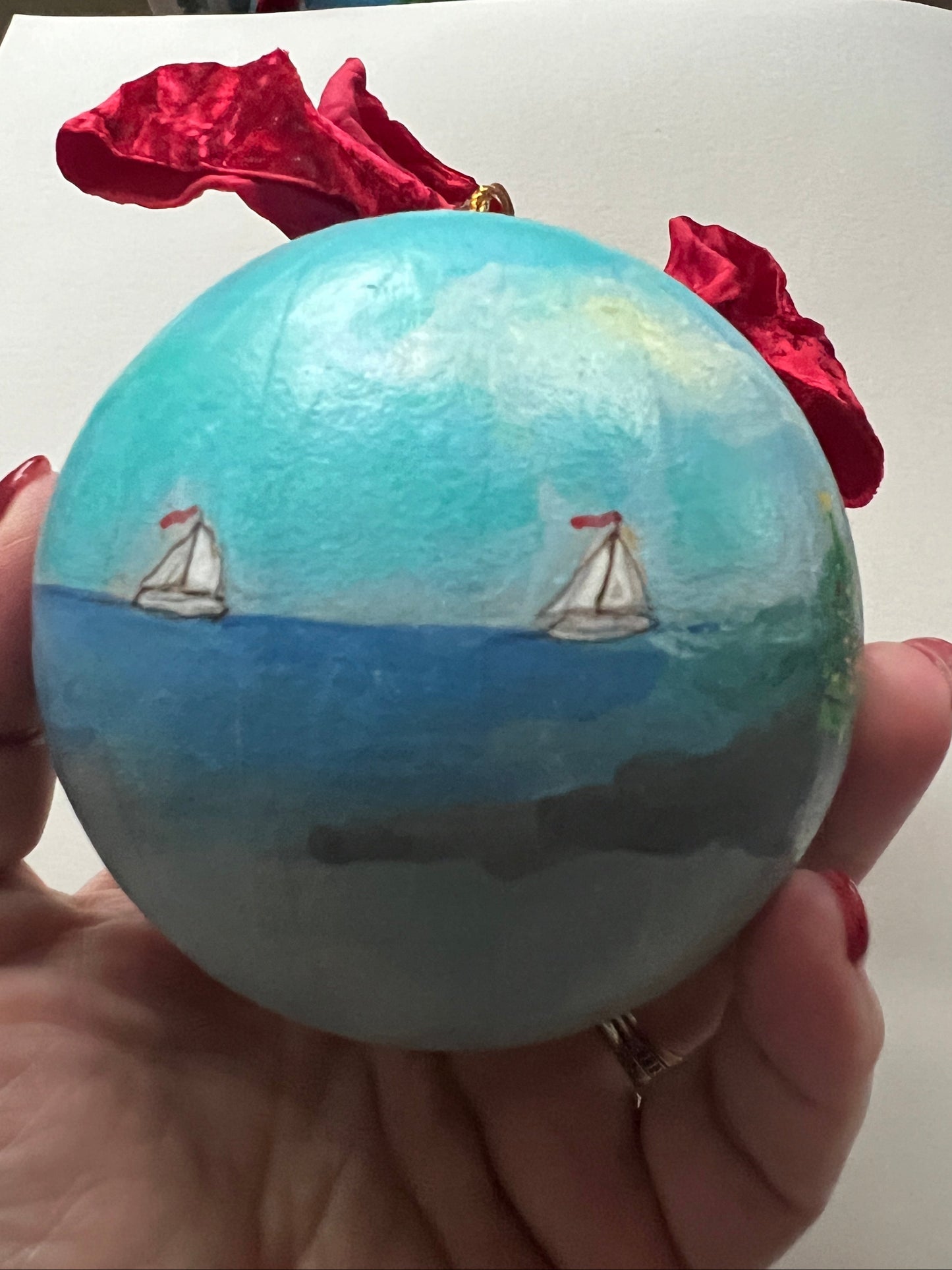 Hand holding a small globe with a sailboat on a white surface.
