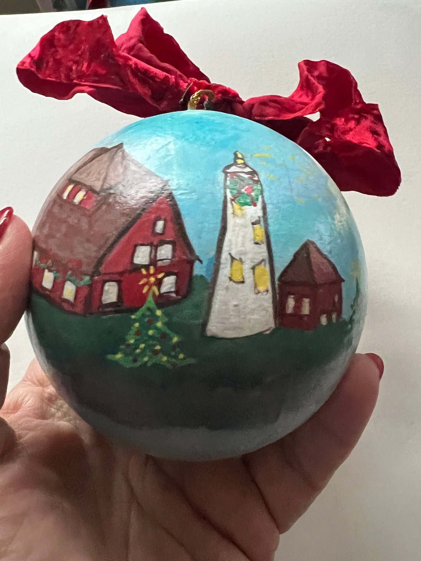 Hand holding a small painted globe with houses on a white surface.