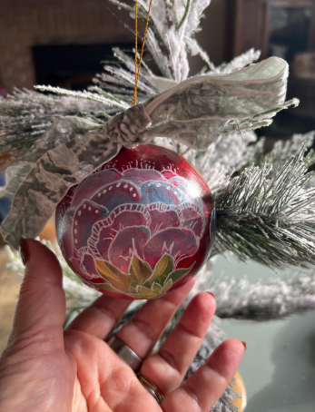 Decorative ornament with floral design held in front of a Christmas tree.