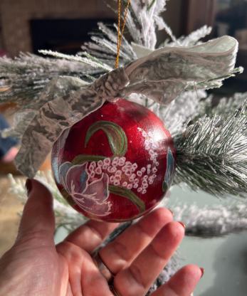 Decorative red ornament with floral design held in front of a Christmas tree.