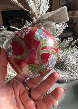 Hand holding a red ornament with floral designs against a Christmas tree background