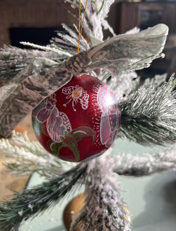 Red Christmas ornament with floral patterns hanging on a decorated tree.