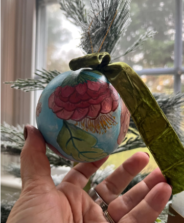 Decorative ornament with floral design held by a hand in front of a window.