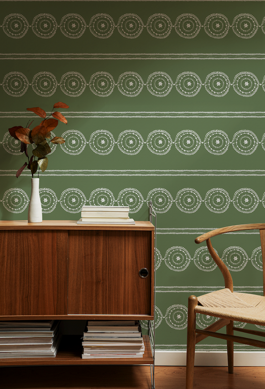 Room interior with wooden cabinet, chair, and vase against a green wall with white geometric pattern.