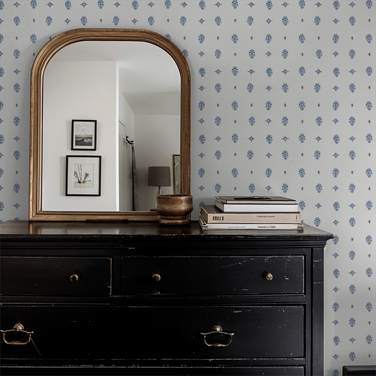 Black dresser with gold mirror and decor against a patterned wall