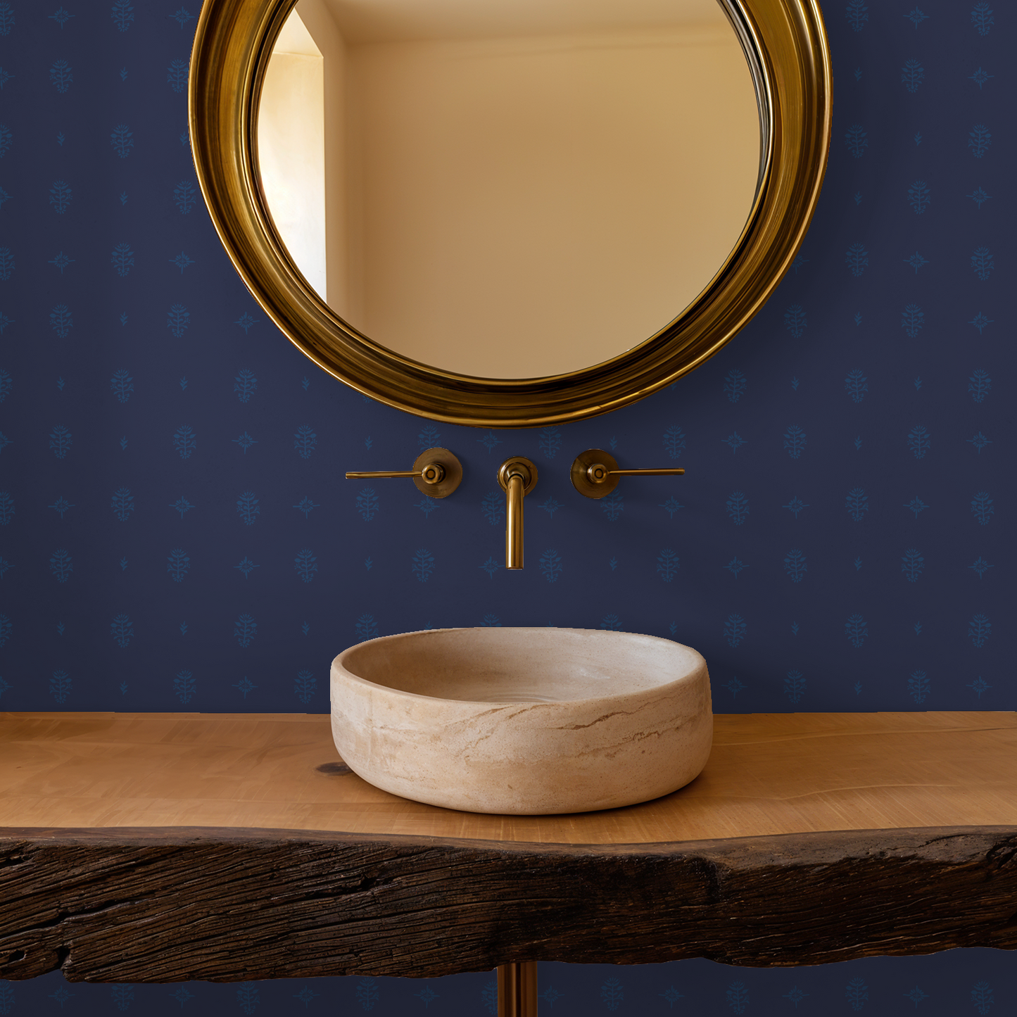 Bathroom setup with a round beige stone sink, gold faucet, and mirror against a blue wall.