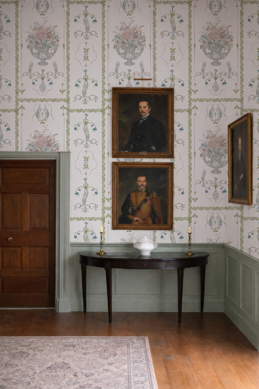 Room with floral wallpaper, portraits on the wall, and a wooden table.
