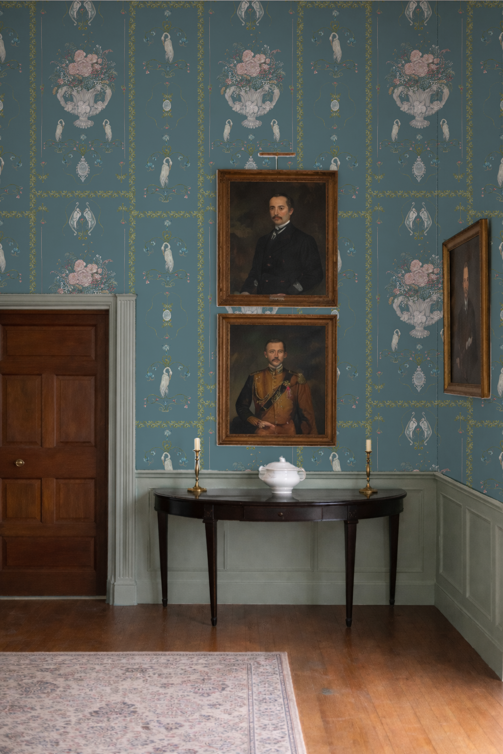 Room with floral wallpaper, portraits on the wall, and a table with a teapot.