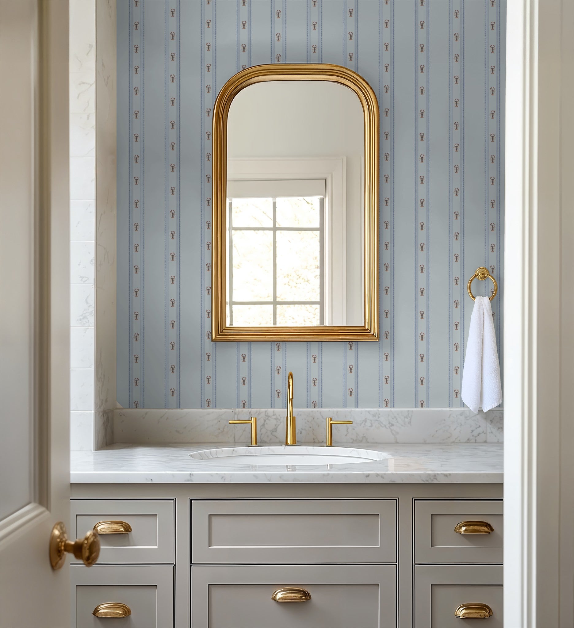 Bathroom with gold-framed mirror, sink, and cabinets against a patterned wall.