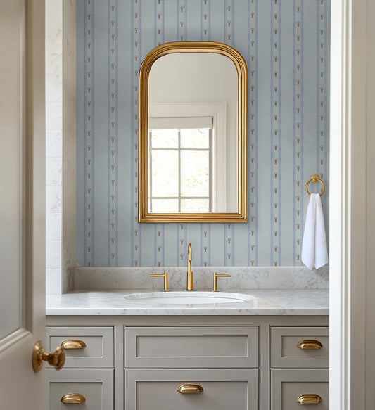 Bathroom with gold-framed mirror, sink, and cabinets against a patterned wall.