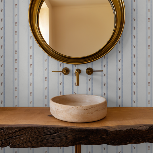 Bathroom vanity with marble sink and gold faucet against striped wallpaper