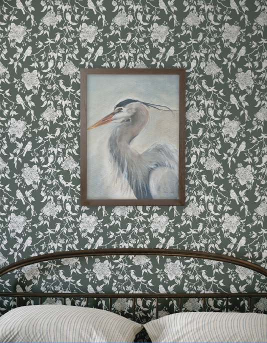 Framed painting of a heron on a wall with floral and bird pattern