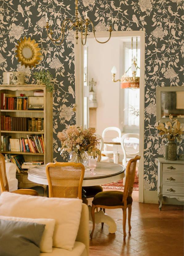 Decorative interior with floral wallpaper, bookshelf, and round table.