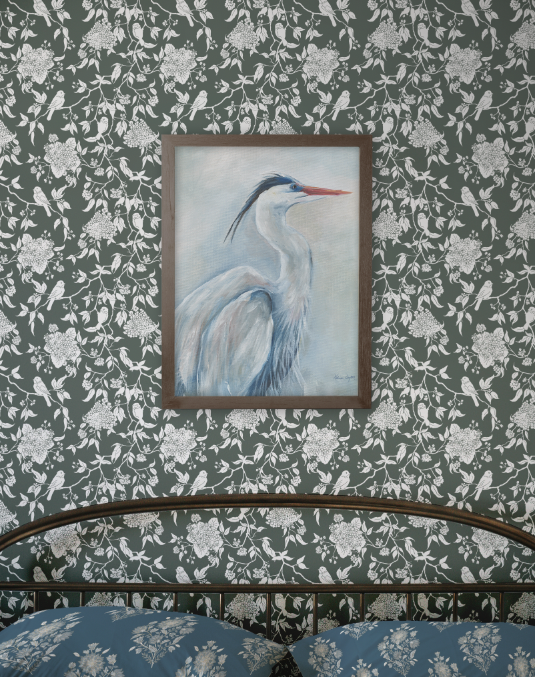 Framed artwork of a heron on a wall with floral pattern