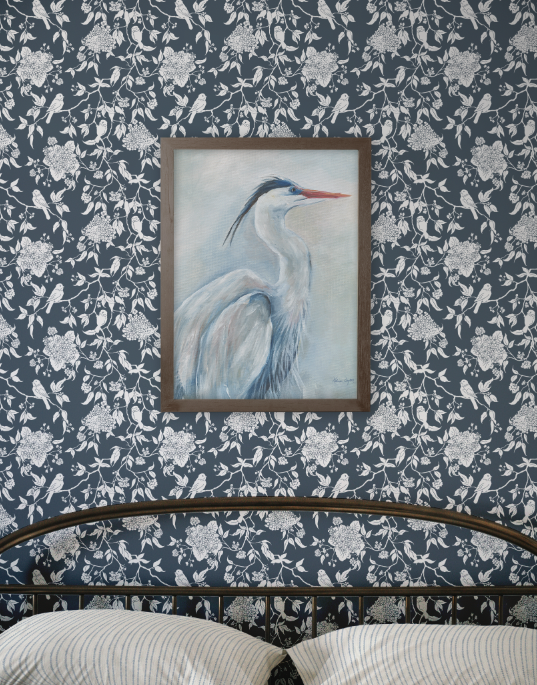 Framed artwork of a heron on a floral-patterned wall.