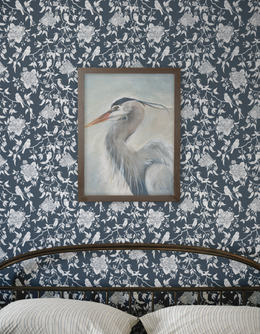 Framed artwork of a heron on a floral-patterned wall.