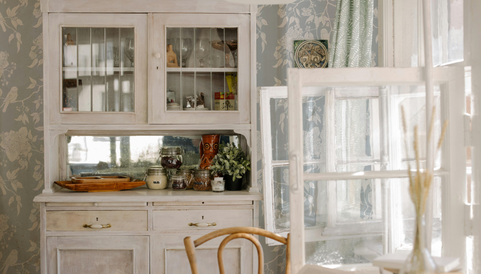 Vintage-style cabinet with glass doors in a room with patterned wallpaper.