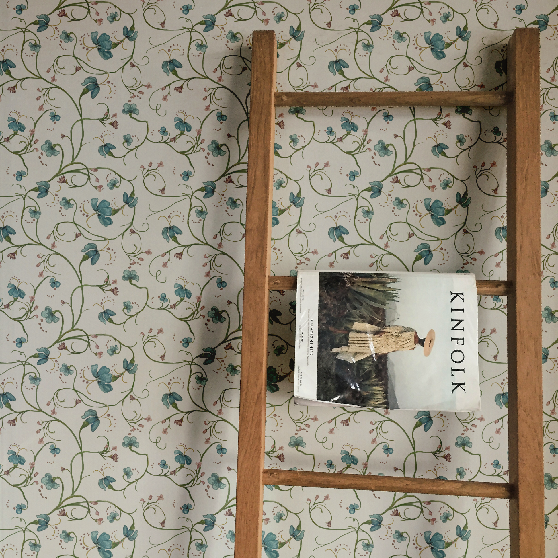 Wooden ladder against a floral wallpapered wall with a book titled 'KINfolk' on it.