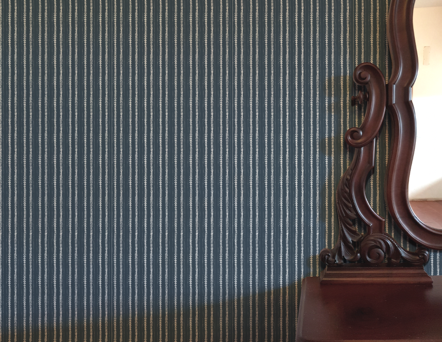 Wooden mirror with intricate carvings against a striped blue and white wall.