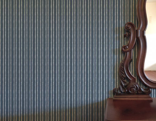 Wooden mirror with intricate carvings against a striped blue and white wall.