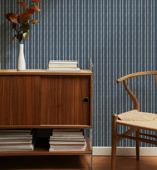 Wooden cabinet with books and a vase against a blue striped wallpaper.