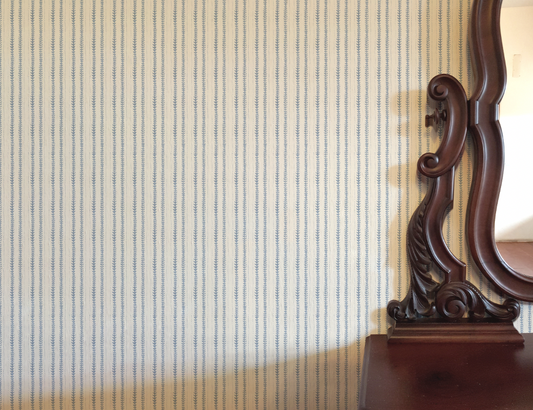 Wooden mirror with decorative frame against a striped wallpaper wall