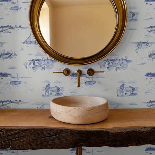 Bathroom vanity with stone sink, gold faucet, and round mirror against a decorative wallpaper.