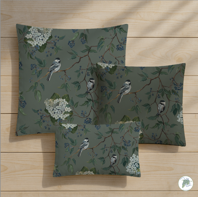 Set of three decorative pillows with bird and floral pattern on a wooden surface
